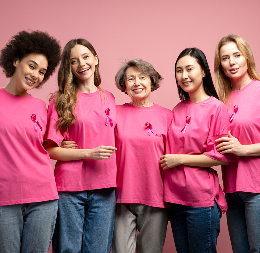 A group of women wearing pink t-shirts with pink ribbons stand together, symbolizing solidarity and support for breast cancer awareness initiatives.