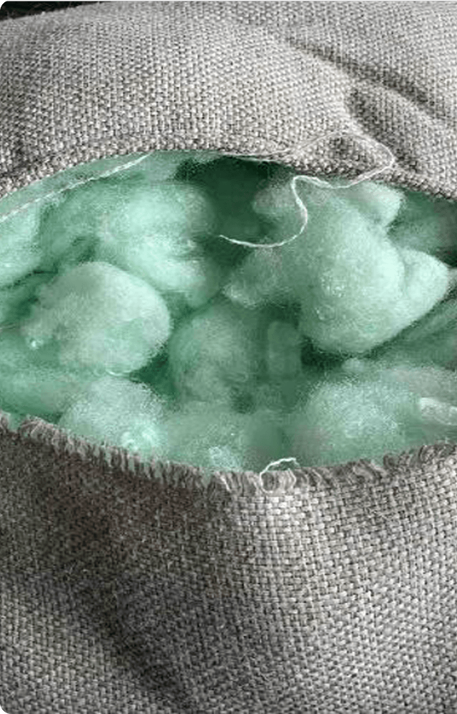 Close-up of a gray fabric pillow with a tear, revealing light green stuffing. The image conveys a sense of wear and the need for repair.