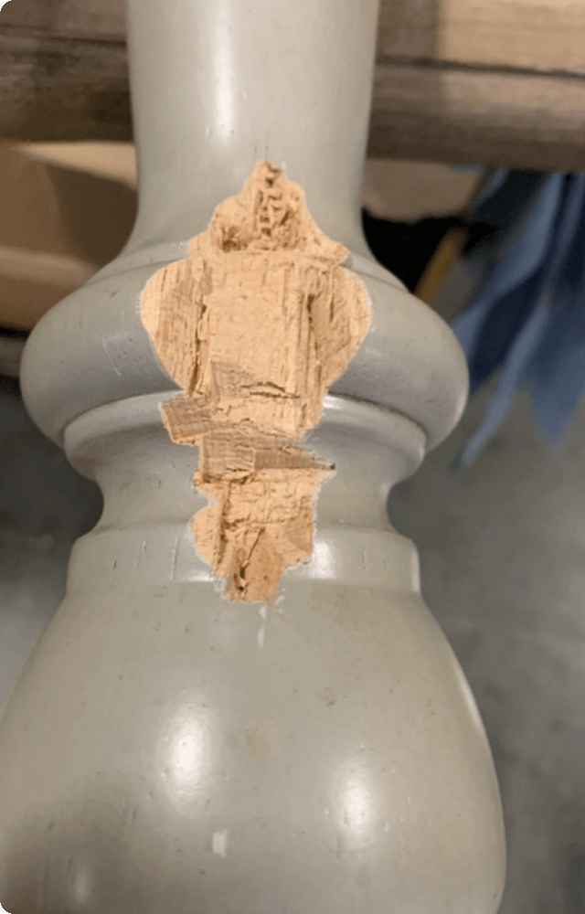 Close-up of a wooden furniture leg with a large, noticeable chip exposing raw wood beneath the paint. The surface looks worn, suggesting wear and tear. A red 'Before' label indicates this is the first picture before a completed transformation.