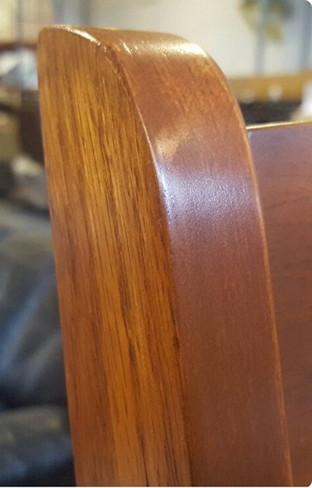 Smooth, polished wooden furniture corner in a soft-focus room. The surface appears shiny and well-maintained, suggesting a recent refinishing.