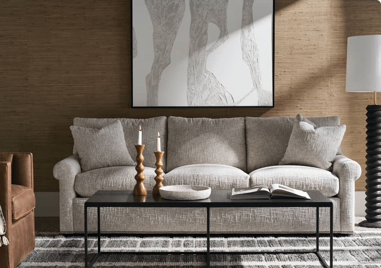 Neutral living room with a gray sofa, black coffee table, candles, open book, and abstract art; a purple circular icon overlays the center cushion.