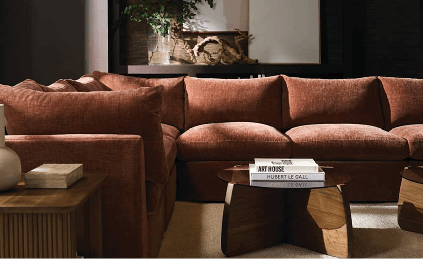 A warm, modern living room features a rust-colored sectional sofa, wooden coffee table, art books, creating a cozy, inviting mood.