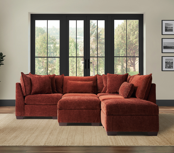 A cozy, rust-colored sectional sofa with two corners and two armless sections set against large windows with a peaceful outdoor view.