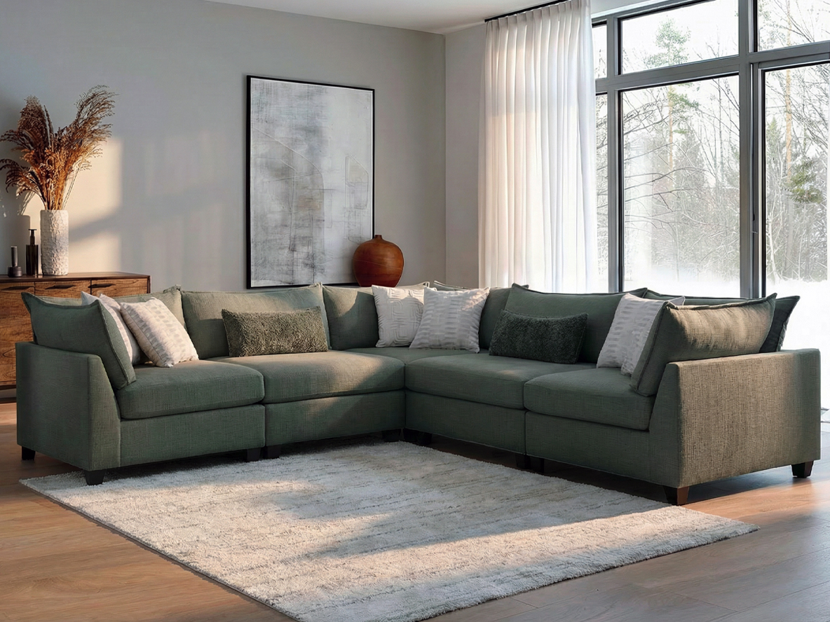 A modern living room features a large gray sectional sofa with multiple cushions, a textured rug, abstract wall art, and sunlight streaming through sheer curtains.