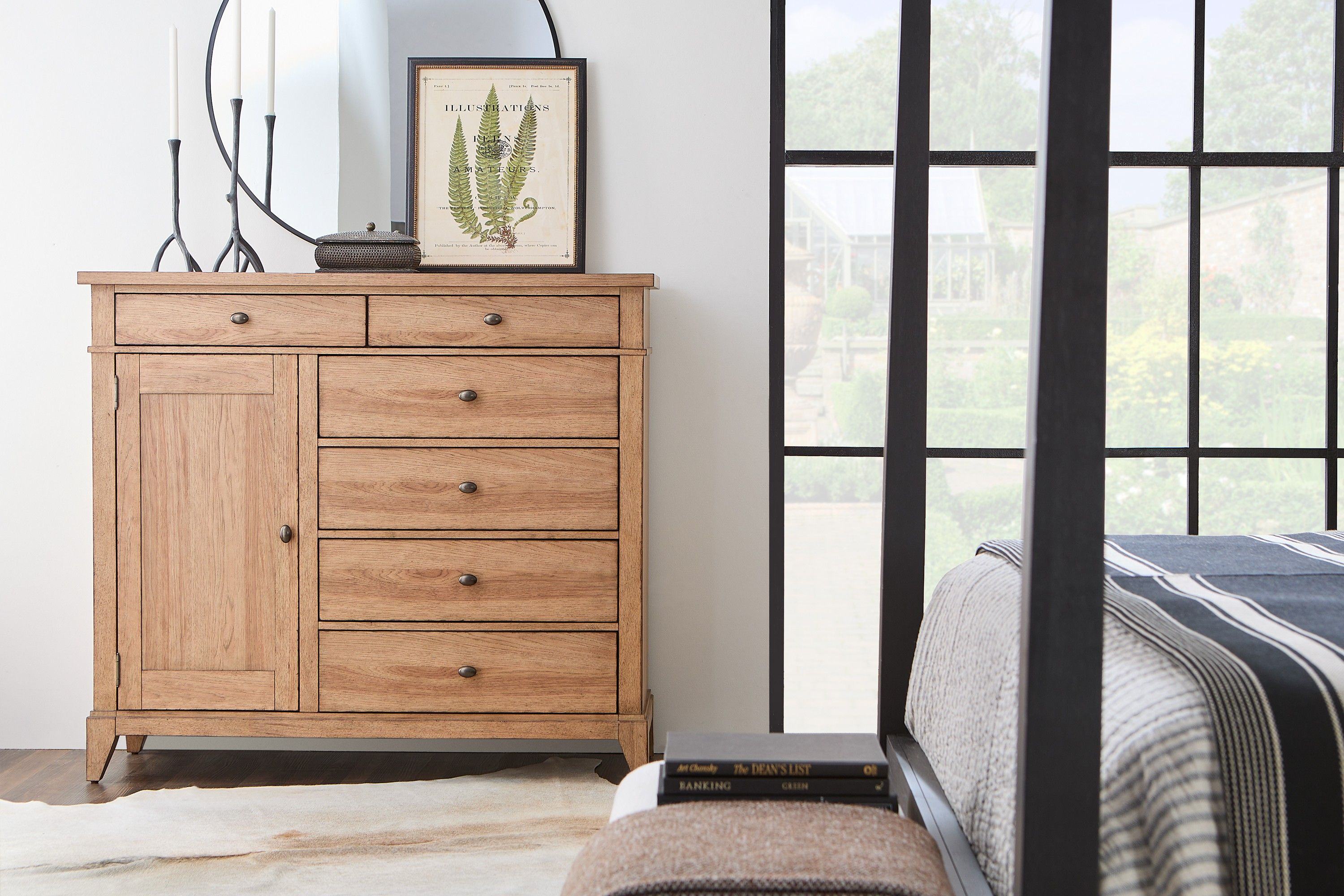 Bright modern bedroom with a neatly made bed, beige and white linens, wood nightstands, framed art, plants, and soft natural light.