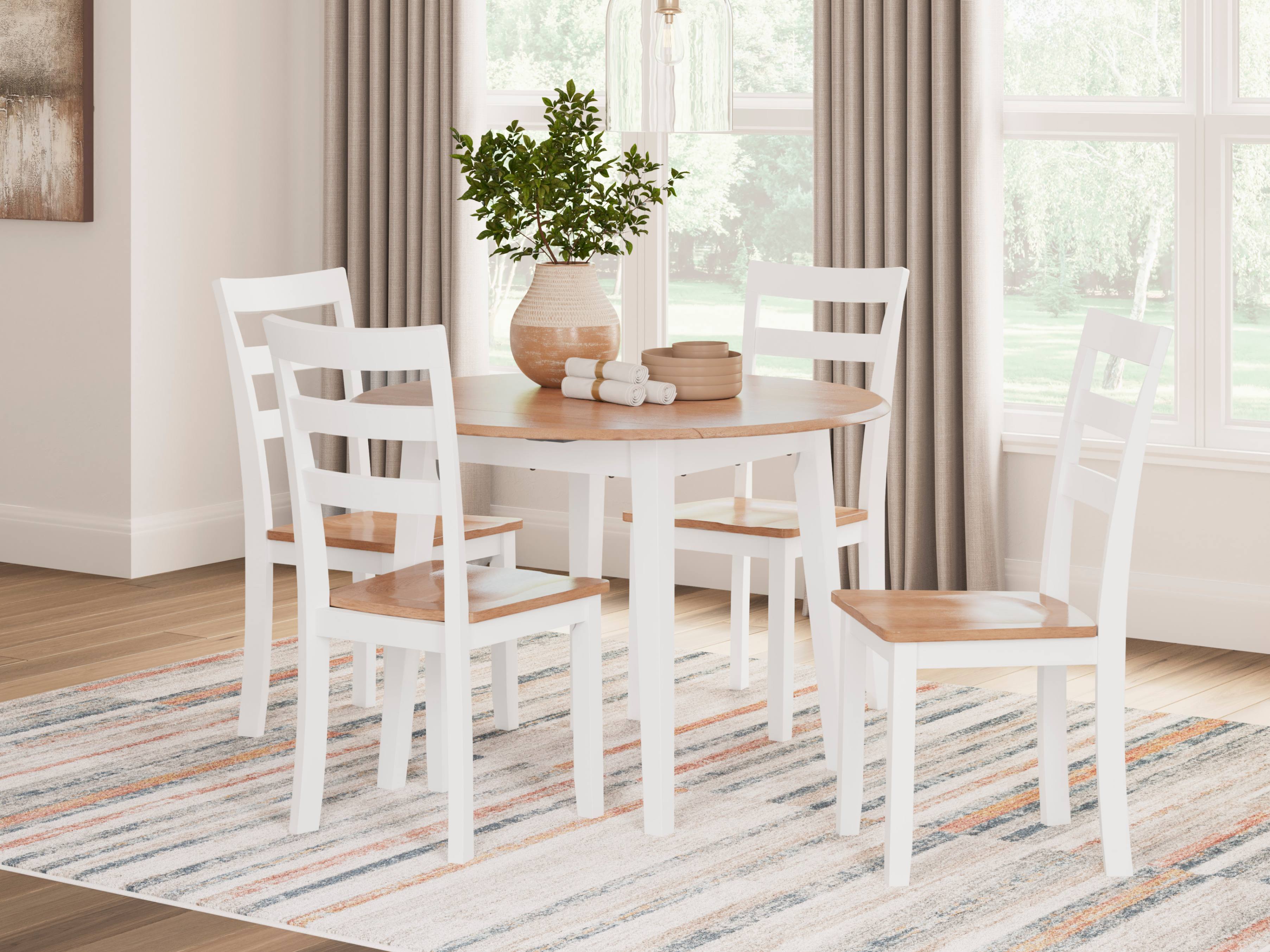 A bright dining nook with a round wood-top table, white chairs, leafy plant, and striped rug sits beside large curtained windows, creating a calm, airy feel.