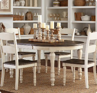 A warm farmhouse dining room features a dark oval table, white turned-leg chairs, glowing candles, and shelves of pottery for a calm, rustic feel.