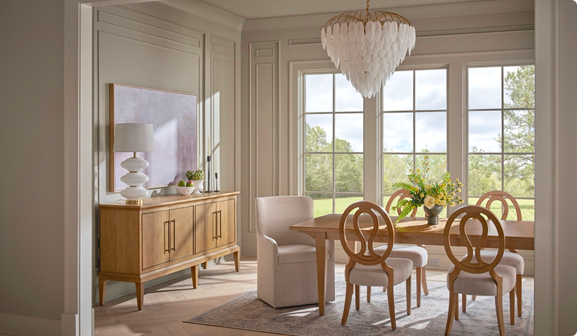 Sunlit elegant dining room with a wooden table, sculptural chairs, sideboard, and feathered chandelier; large garden-facing windows create a calm, airy mood.