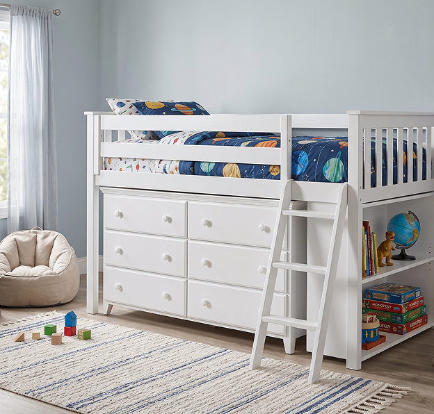 White children’s loft bed with a six-drawer dresser, ladder, and space-themed bedding; books and toys below, beside a bright window in a calm playroom.