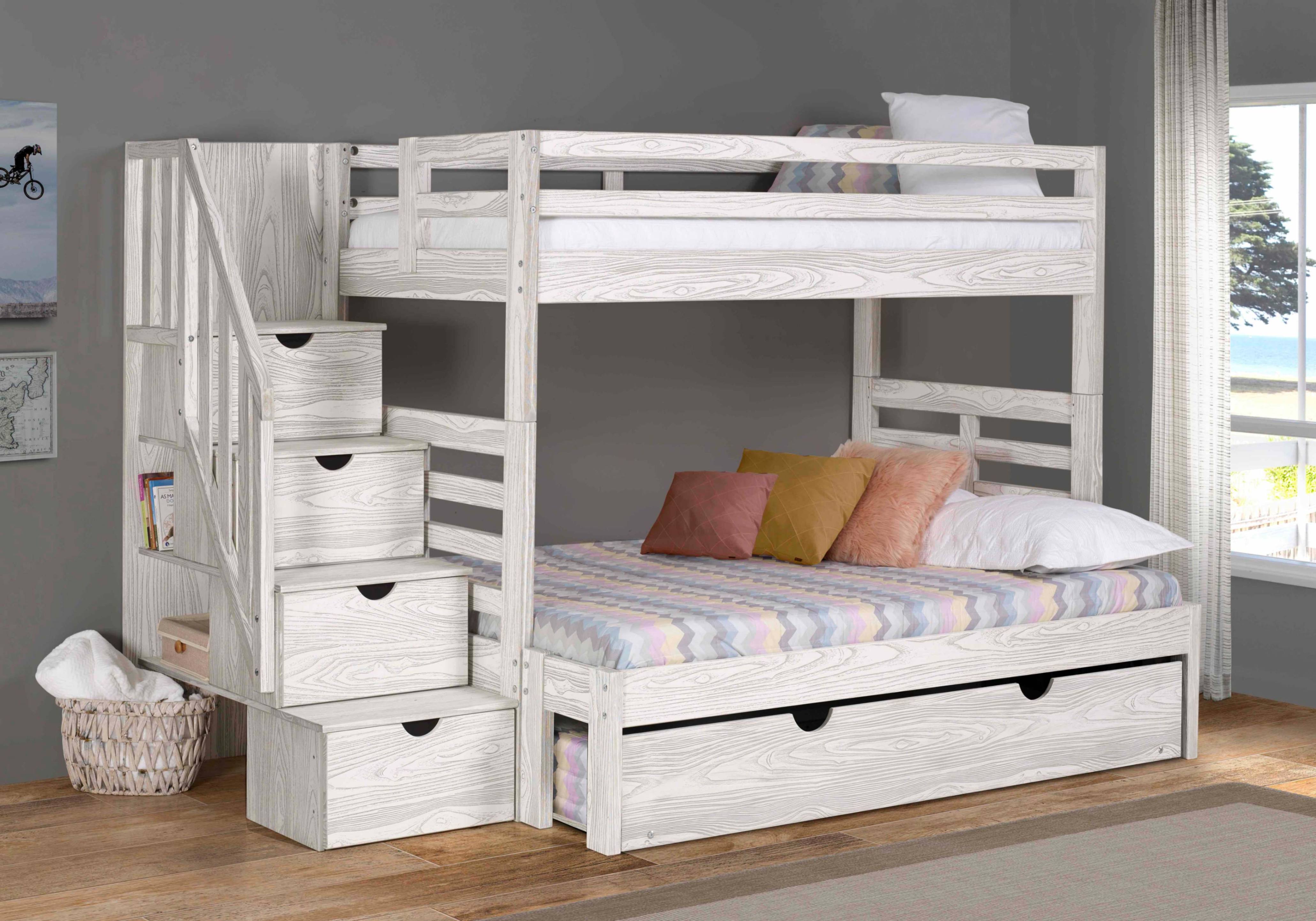 Whitewashed wooden bunk bed with built-in staircase drawers and a lower trundle bed, dressed in pastel bedding and pillows in a bright, cozy bedroom.