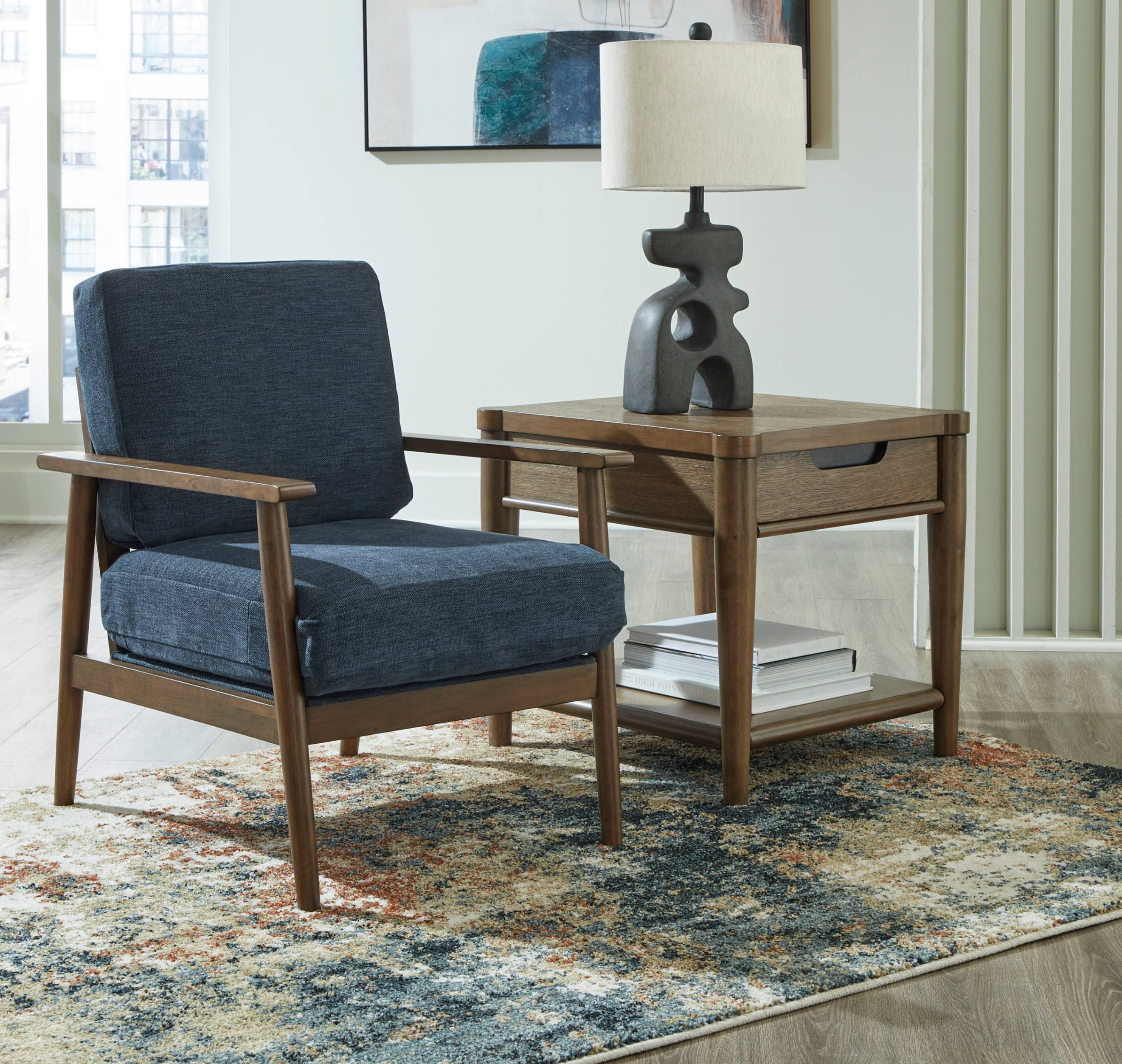 Mid-century modern reading nook with a navy armchair, wooden side table, sculptural lamp, books, and patterned rug in a bright, cozy room.