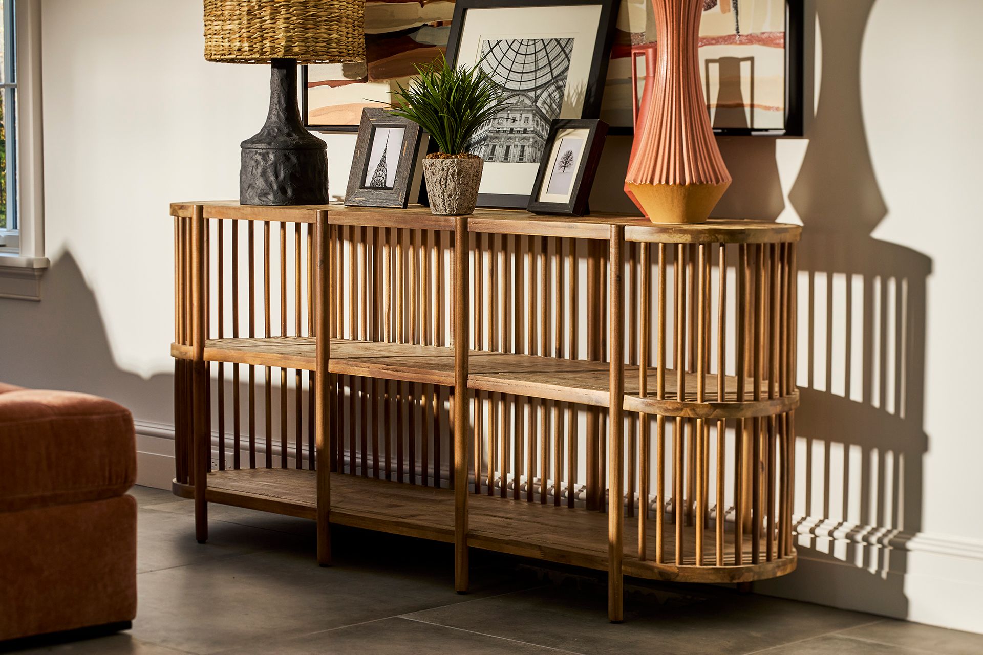 Sunlit wooden slatted console table with framed art, plants, and lamps in a warm, stylish living room; dramatic shadows create a cozy mood.