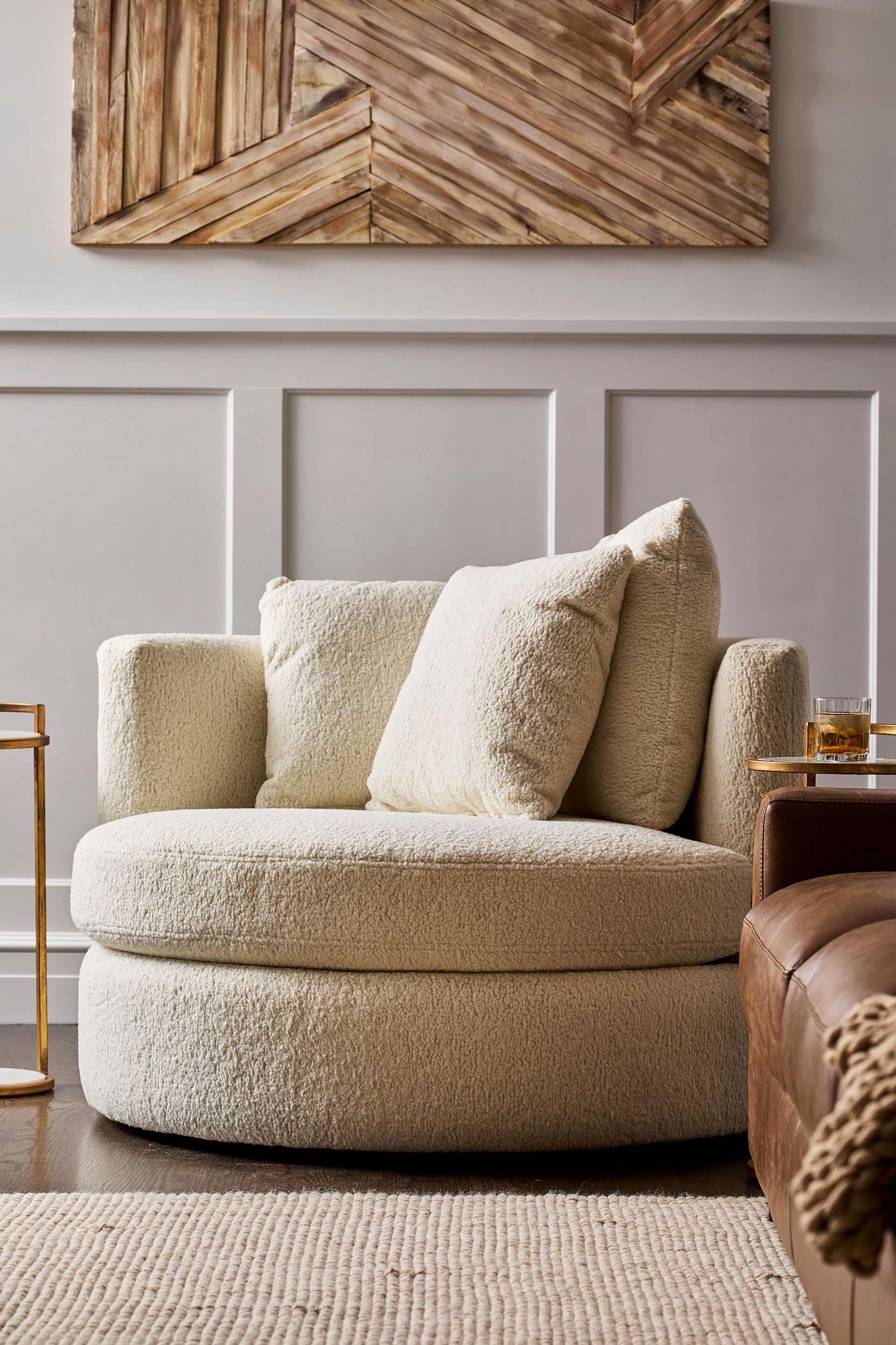 Cozy cream boucle lounge chair with plush pillows, set against paneled walls and rustic wood art; warm neutral tones create a serene feel.