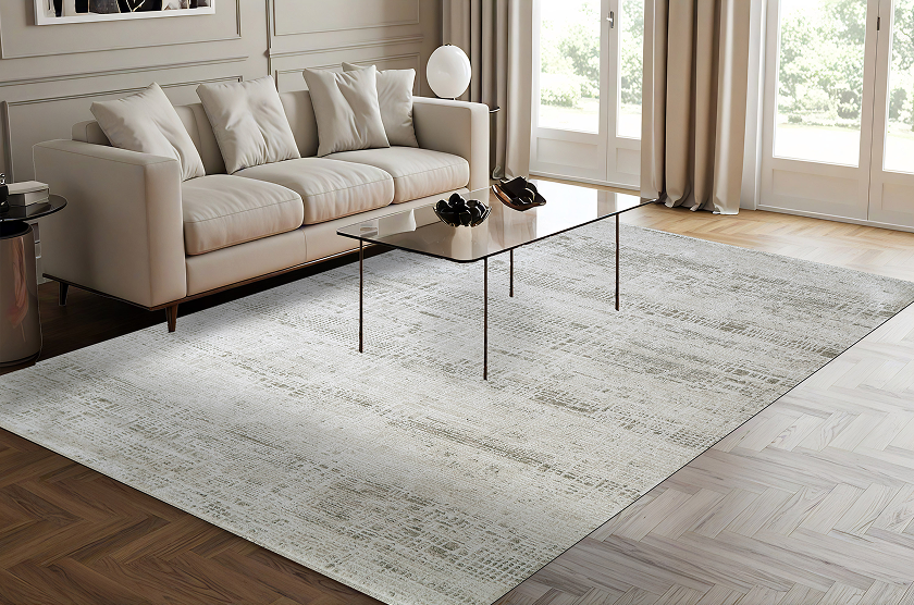 A neutral living room features a beige sofa, slim black coffee table, and pale patterned rug, with sunlight through tall windows creating a calm, airy feel.